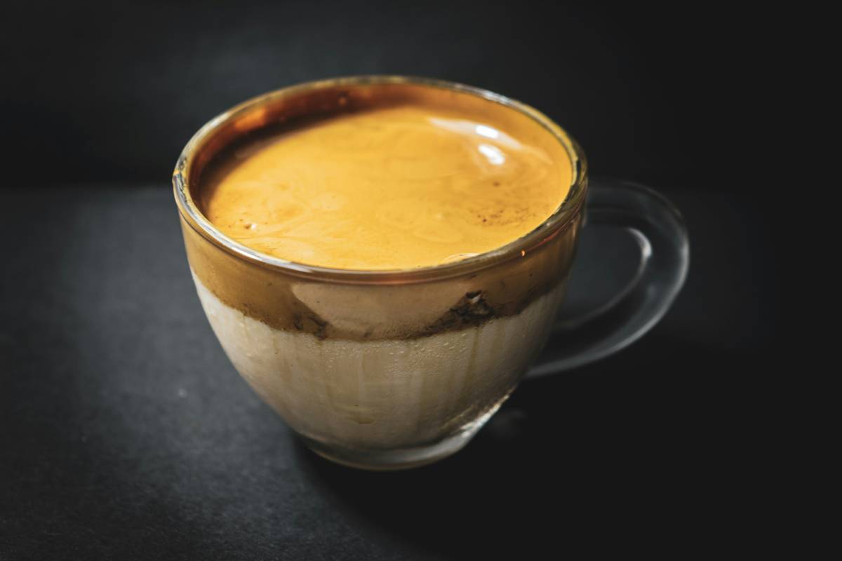 A glass of golden milk with fresh turmeric root beside it on a wooden table.