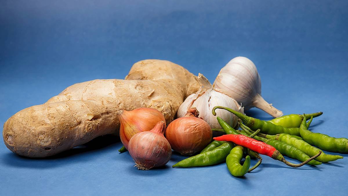 A bowl of fresh turmeric root beside powdered turmeric and a spoon